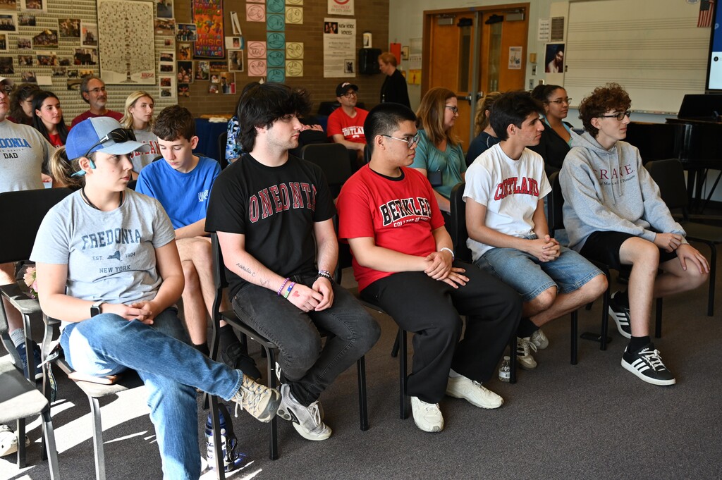 Five students sit in chairs at the front of the room.