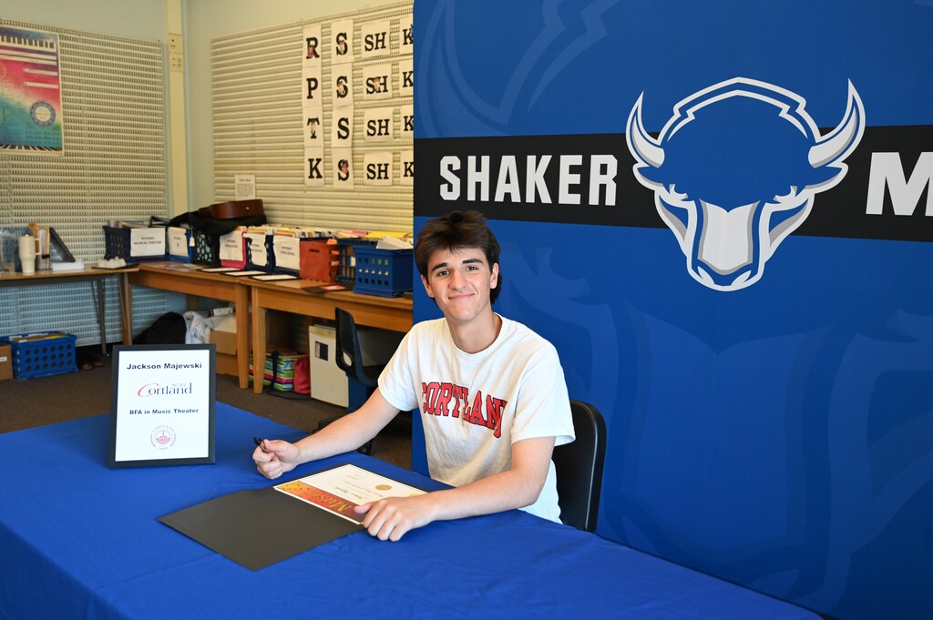 A student sits at a table and poses after signing.