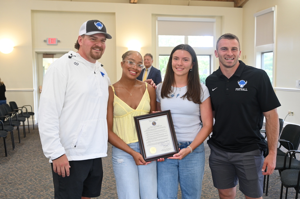 Two coaches and two players pose with the proclamation from Mr. Crummey.