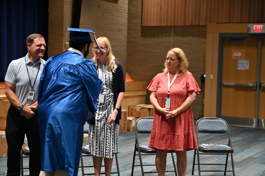 A graduate in cap and gown shakes the hands of district administrators after receiving his diploma.