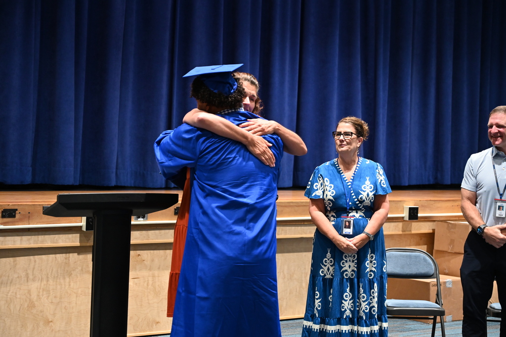A graduate in cap and gown hugs a teacher.
