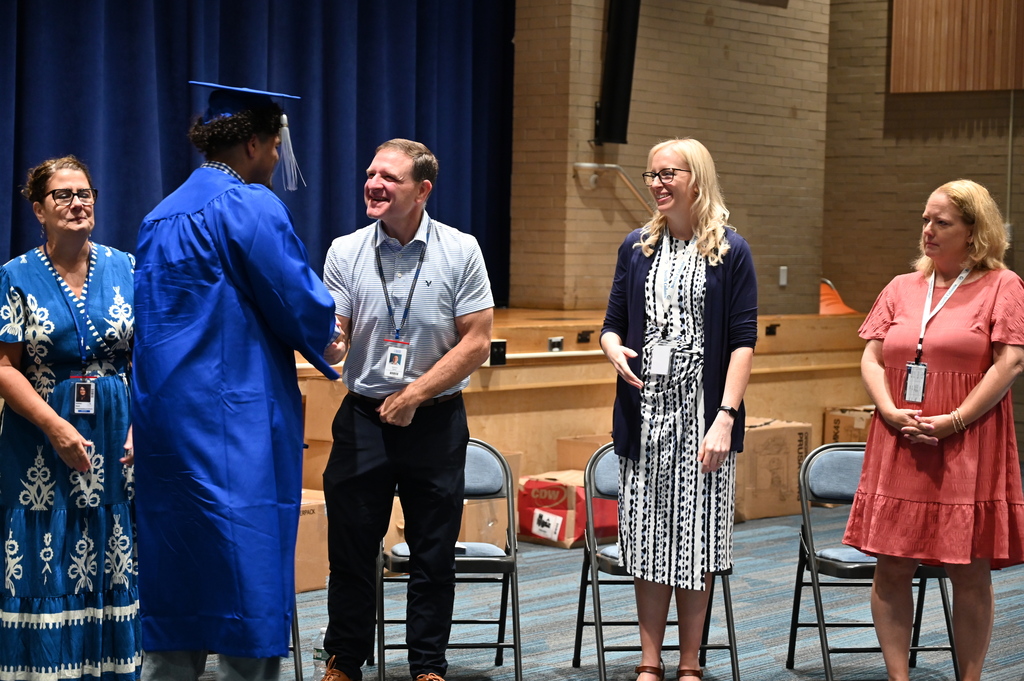 A graduate in cap and gown shakes the hands of administrators.