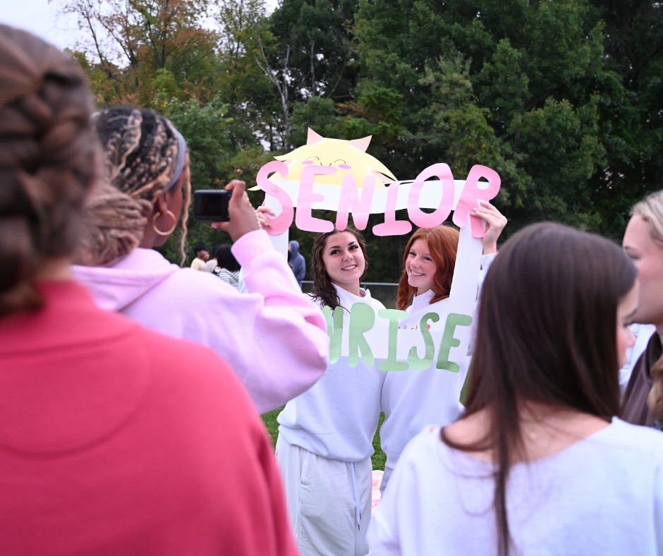Seniors in front of the sunrise holding up a sign getting their picture taken