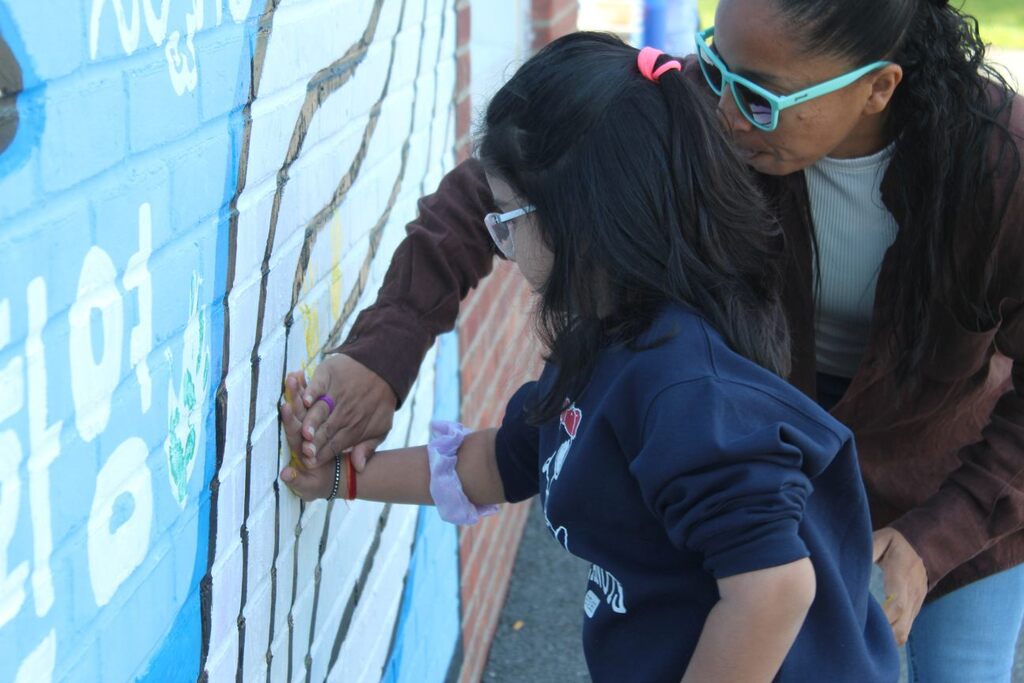 student placing their hand on the wall with the help of a teacher