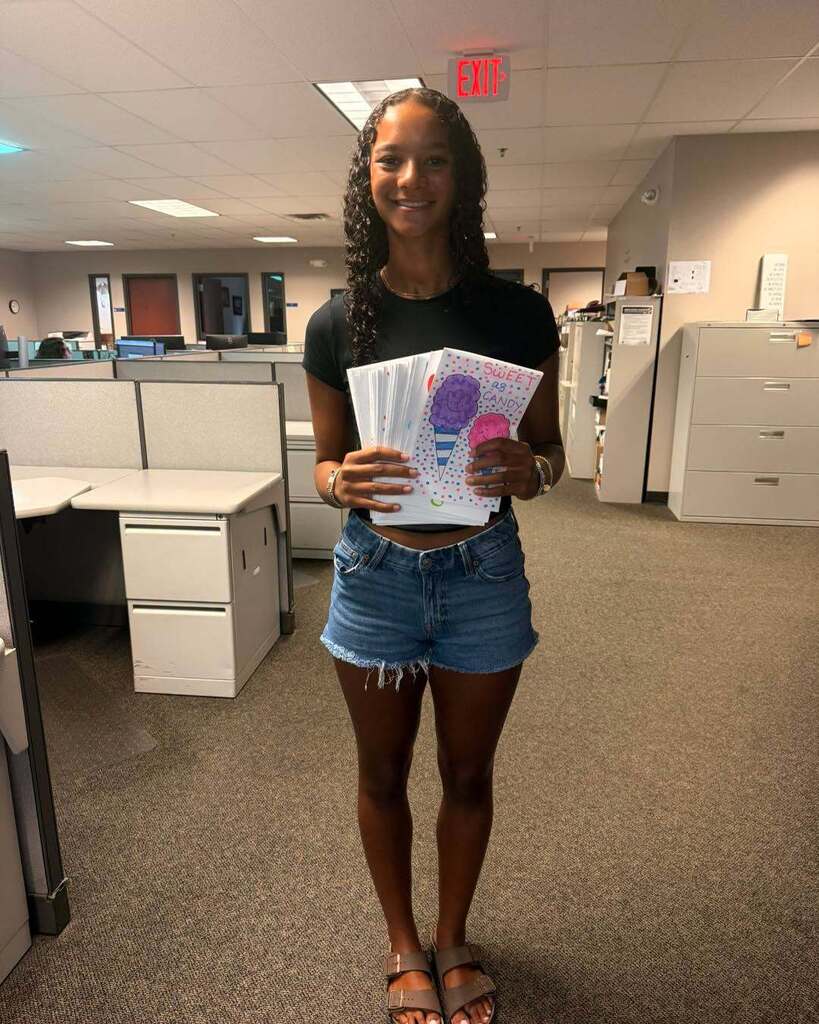 An image of a student standing in an office space holding more than a dozen handmade cards.