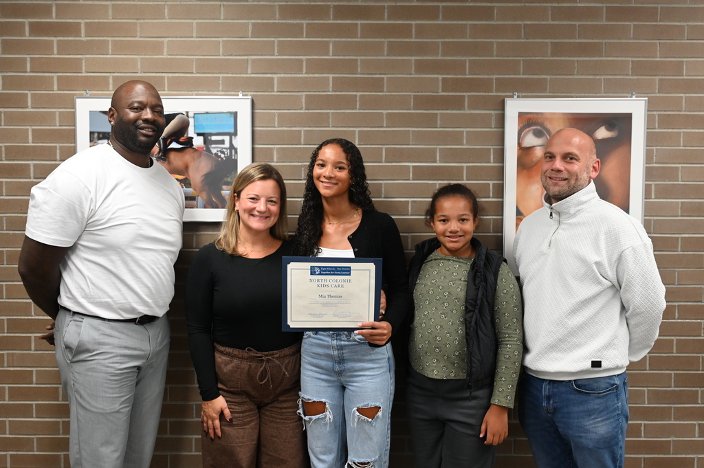 A student stands proudly with her family as she holds her Kids Care certificate.