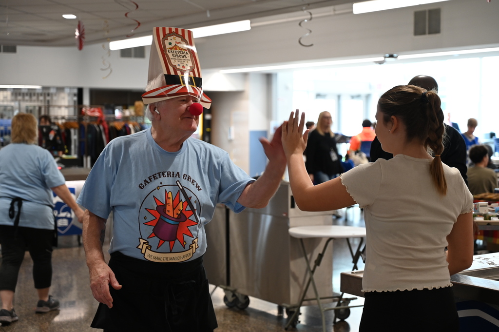 ​Shaker Middle School Cafeteria worker wearing clown noses and circus hats gives SMS student a high five