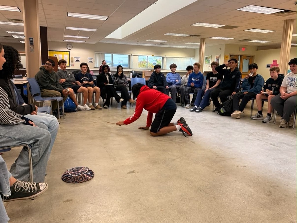 German club playing a game for octoberfest with students sitting in chairs around a student in the middle