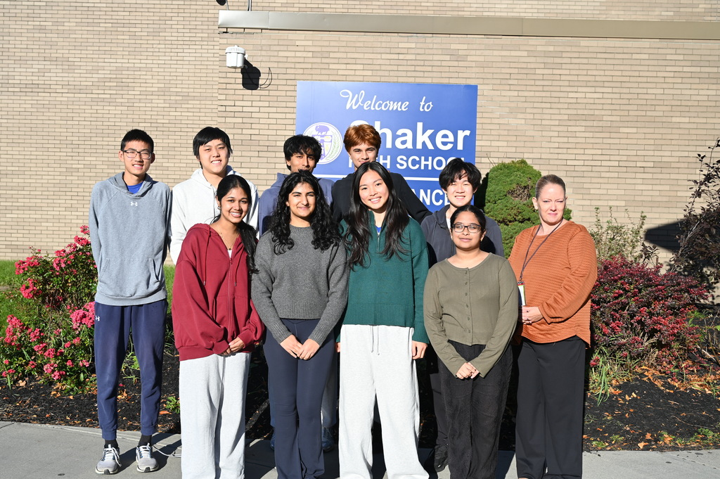 Nine National Merit Scholarship Semifinalist students pose with Principal Crystal Fox in front of the Shaker High School sign.