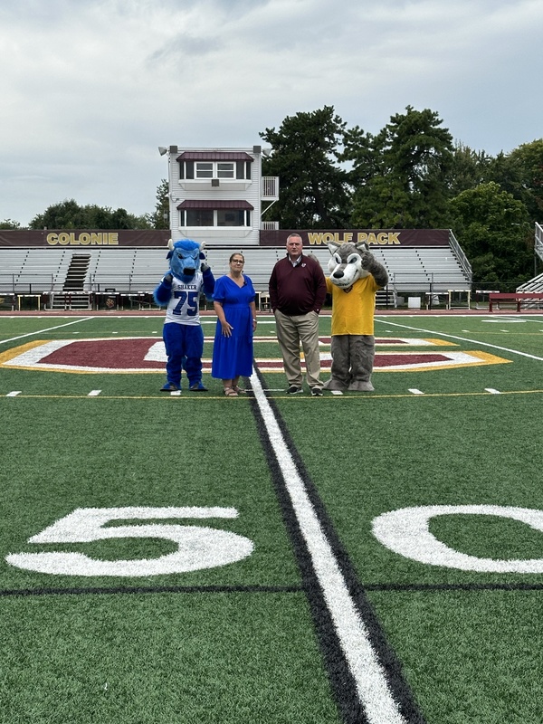Bryson the Bison, Kathy Skeals, South Colonie Superintendent and Wolfie from South Colonie standing on a football field
