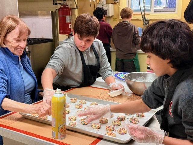 german club students making christmas cookies, group of three students putting cookies on a tray