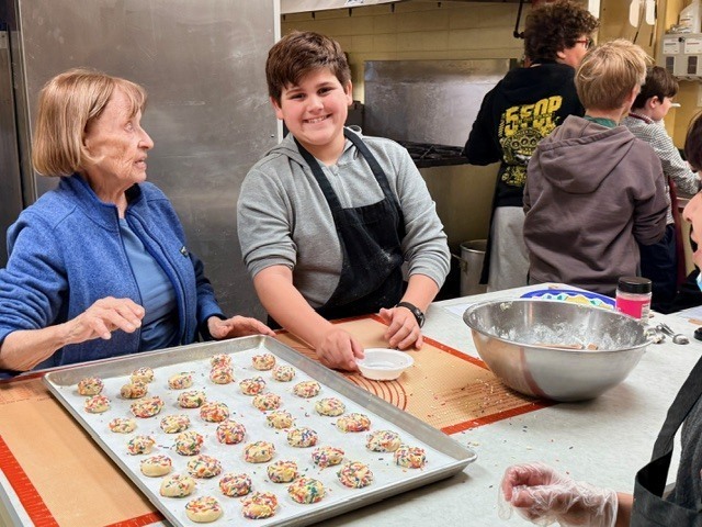 german club student smiling at the camer as he puts cookies on a baking sheet