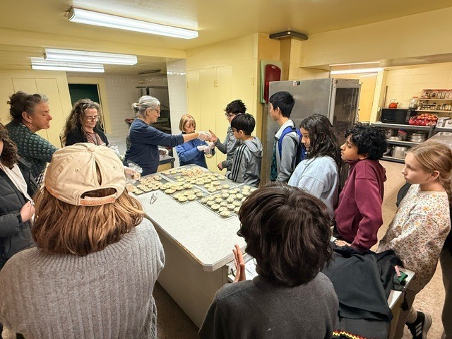 group of german club sms students standing around the table as they learn how to make christmas cookies