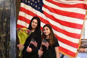 Marianna Kilinkarova Zahopoulos and her daughter Andriana pose in front of the American flag.
