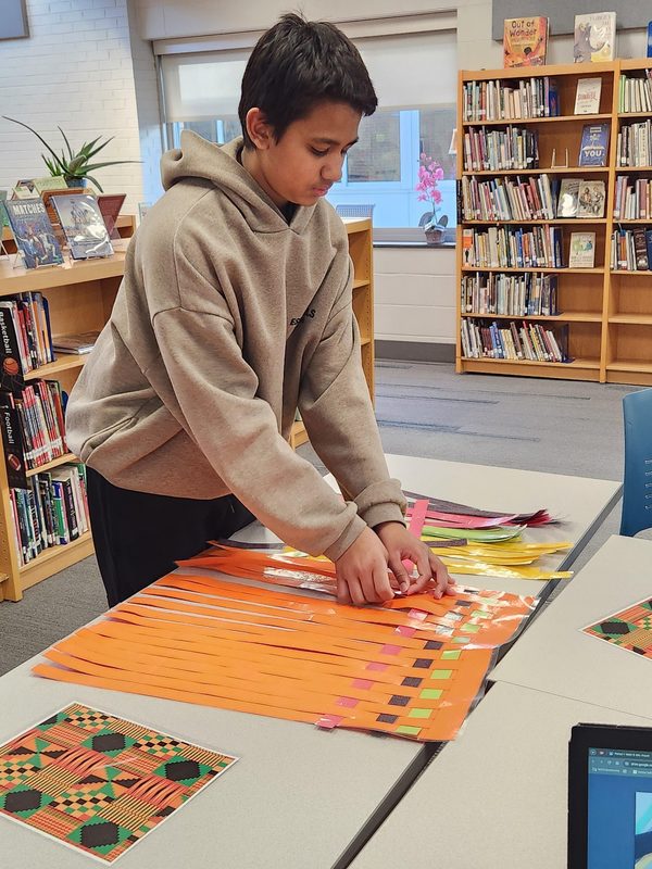 A student creates a kente cloth while participating in stations about math transformations.