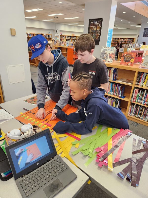 Students work together to weave fabric to create a kente cloth.