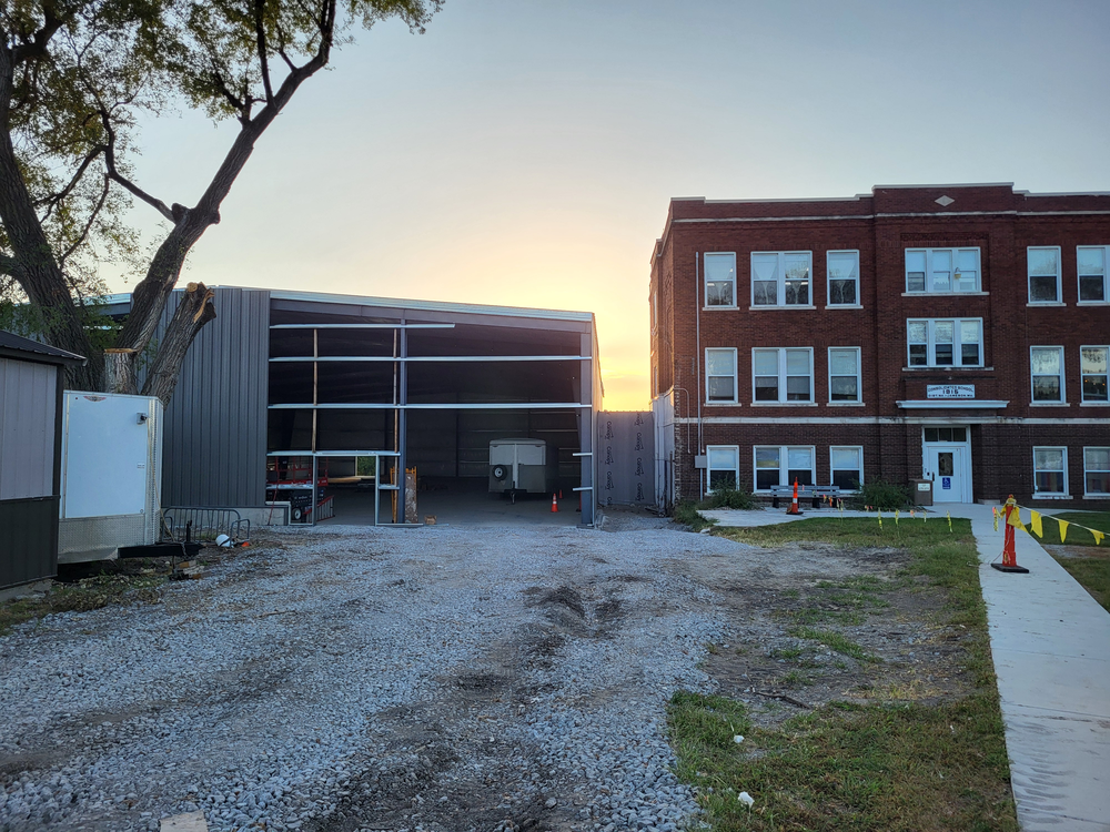photo of the in progress gym, with sun rising behind it, set next to the original 1915 North daviess building