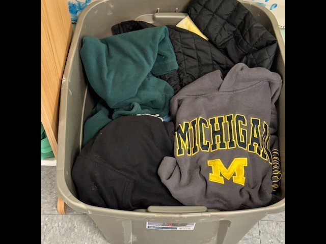 A storage box filled with various clothes, including a Michigan sweatshirt. The box is on a wooden floor.