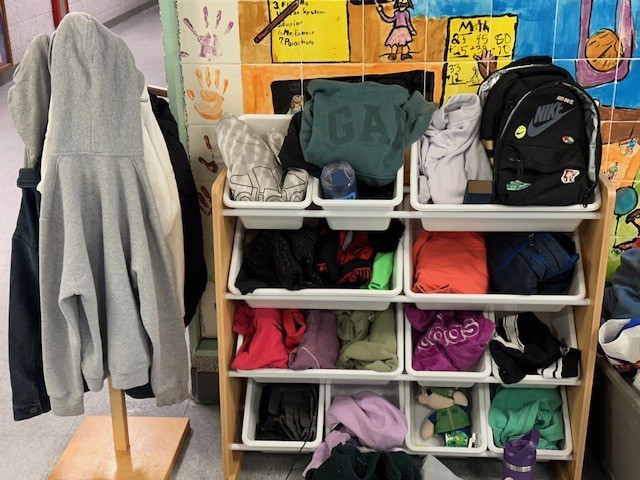 A wooden shelving unit with multiple drawers filled with various clothes, a backpack, and a gray coat.