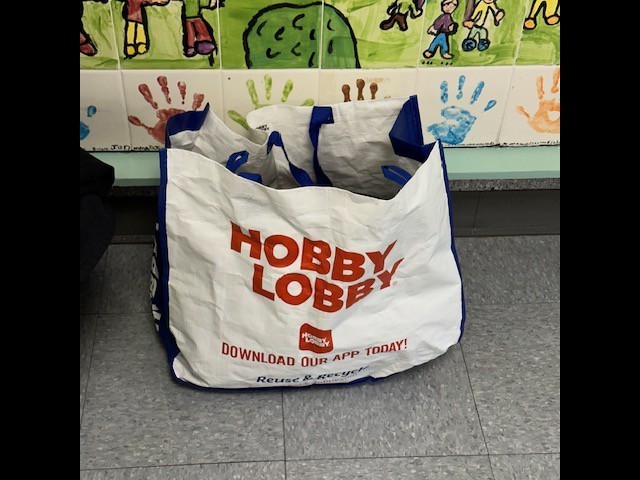A white bag with blue trim and "Hobby Lobby" printed on it, filled with items. A colorful wall mural behind.