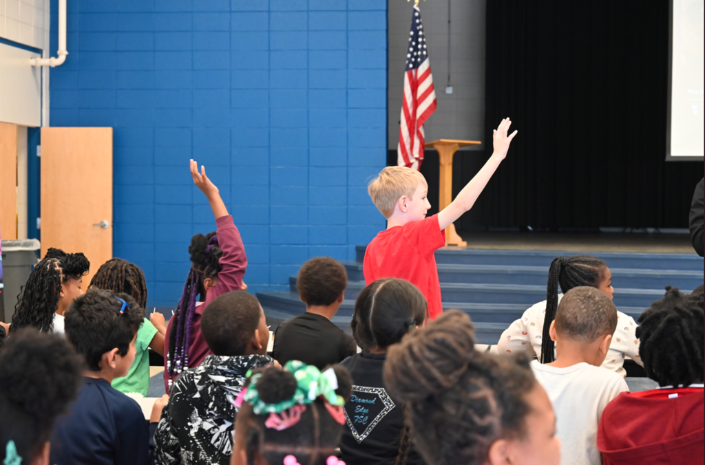 Students raising their hands in a filled school auditorium