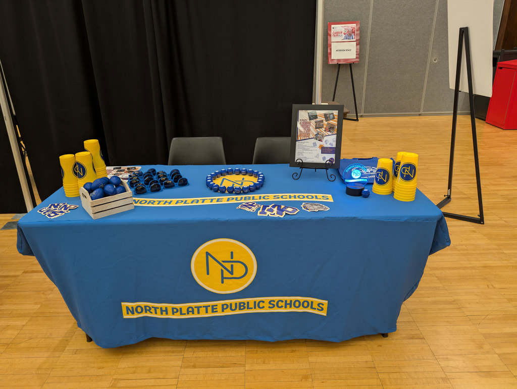 NPPS table at UNL Career Fair. Table decorated with Promotional items, flyers, and the gold NP interlocked logo on blue table.