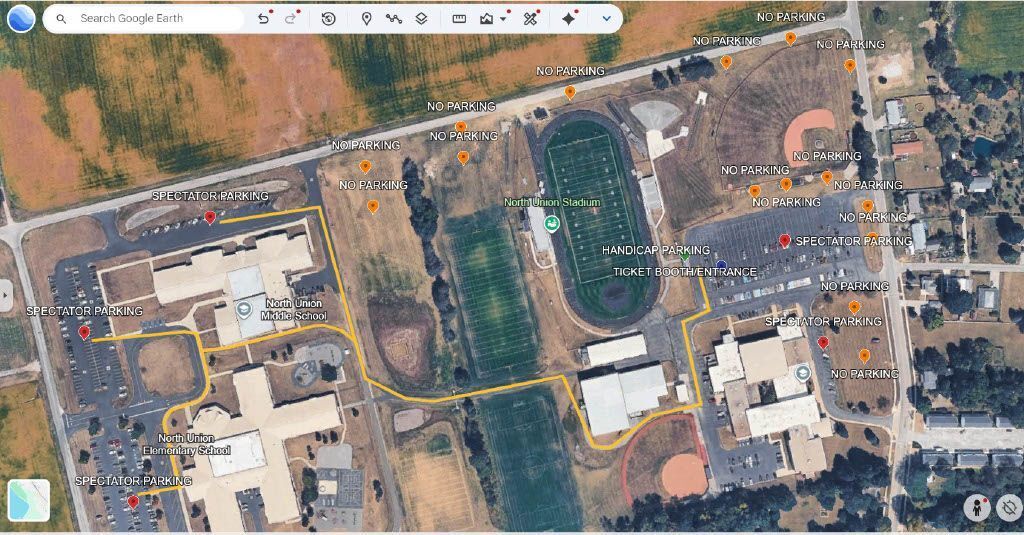 Aerial view of a campus with a football field, a baseball field, and several buildings. A yellow line marks a path.
