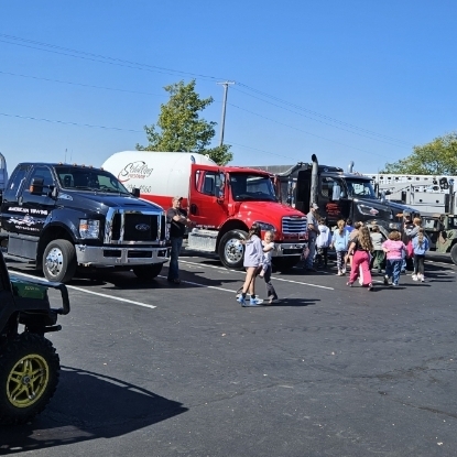 Multiple trucks parked in a lot with children walking among them on a sunny day.