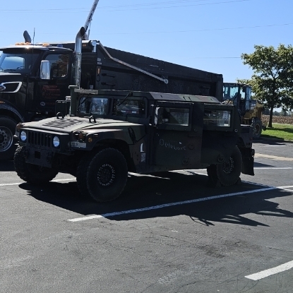 Military vehicles parked on a road. One is an HMMWV with a large exhaust pipe.