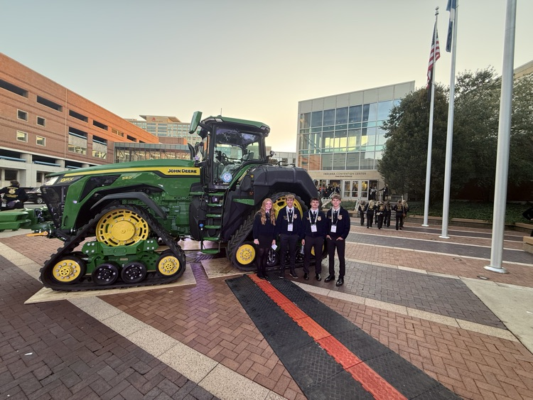 Five people pose in front of a large green and yellow tractor on a paved area.