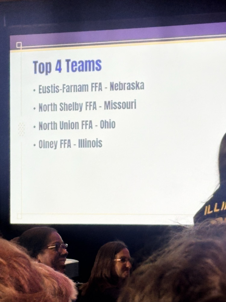 A presentation screen displays a list of teams, including Eustis-Farnam FFA from Nebraska, and several people seated.