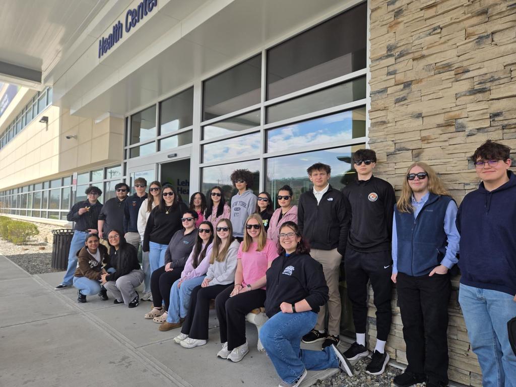 A group of students standing against windows and a brick wall. All wearing sunglasses.