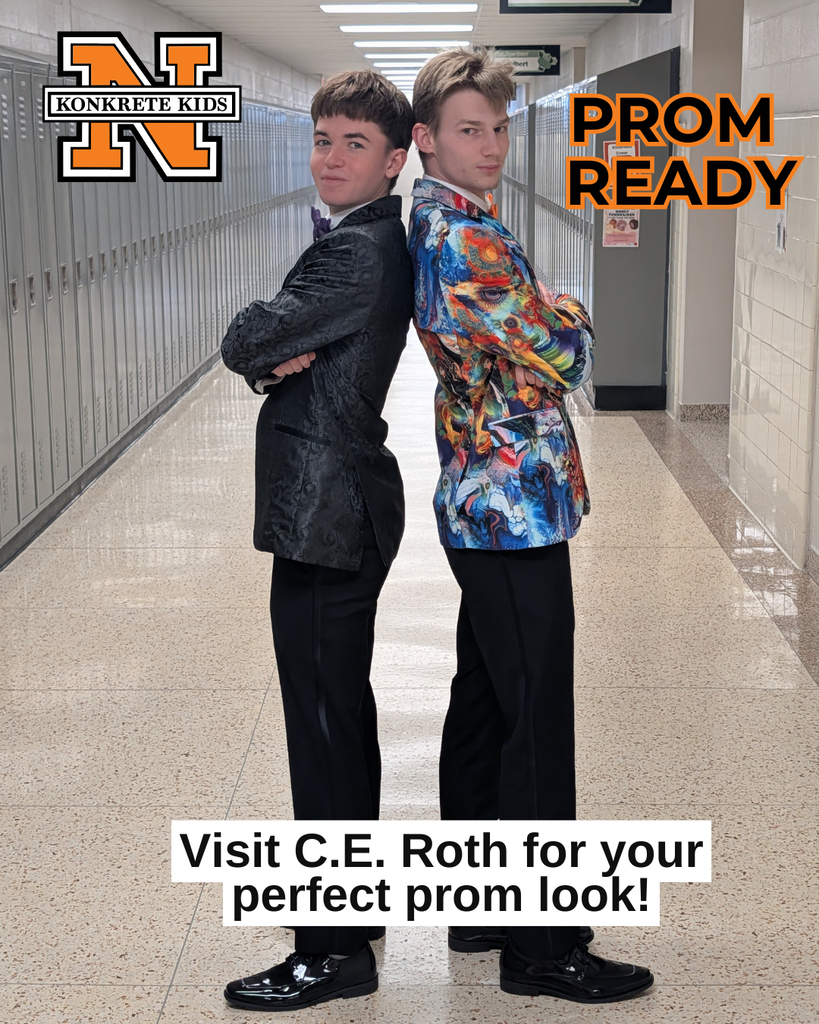 Two students standing in a hall back to back with arms crossed modeling their tuxedos. One in grey and the other in a multi color jacket.
