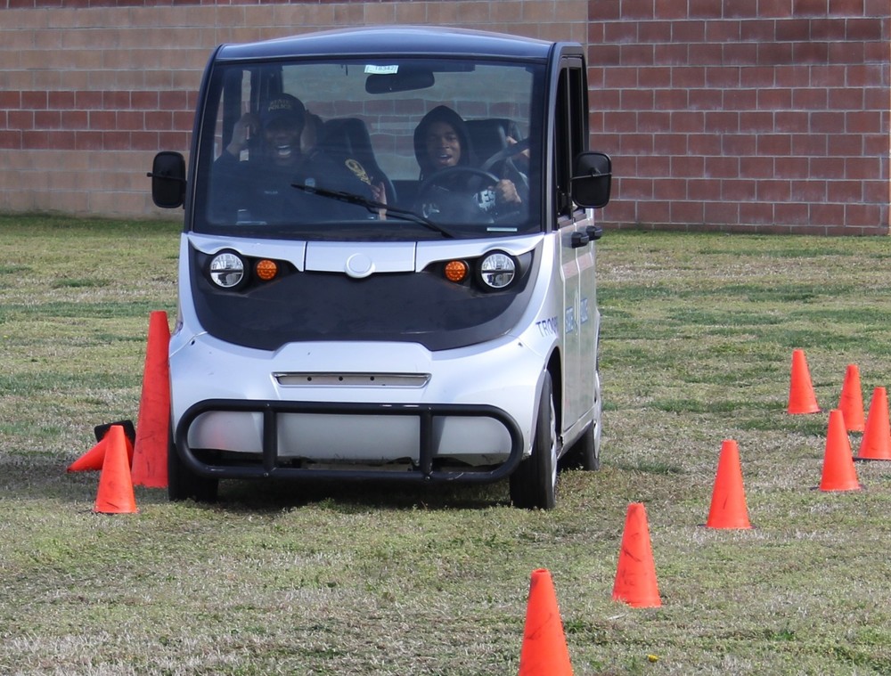 student driver driving covered golf cart with officer in the front passenger seat, lookuing scared, due to impairment. This was a safety simulation exercise.