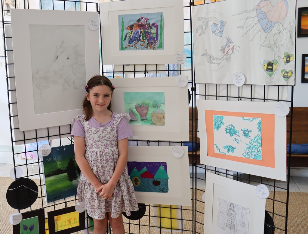student poses with her artwork that is displayed in the art gallery