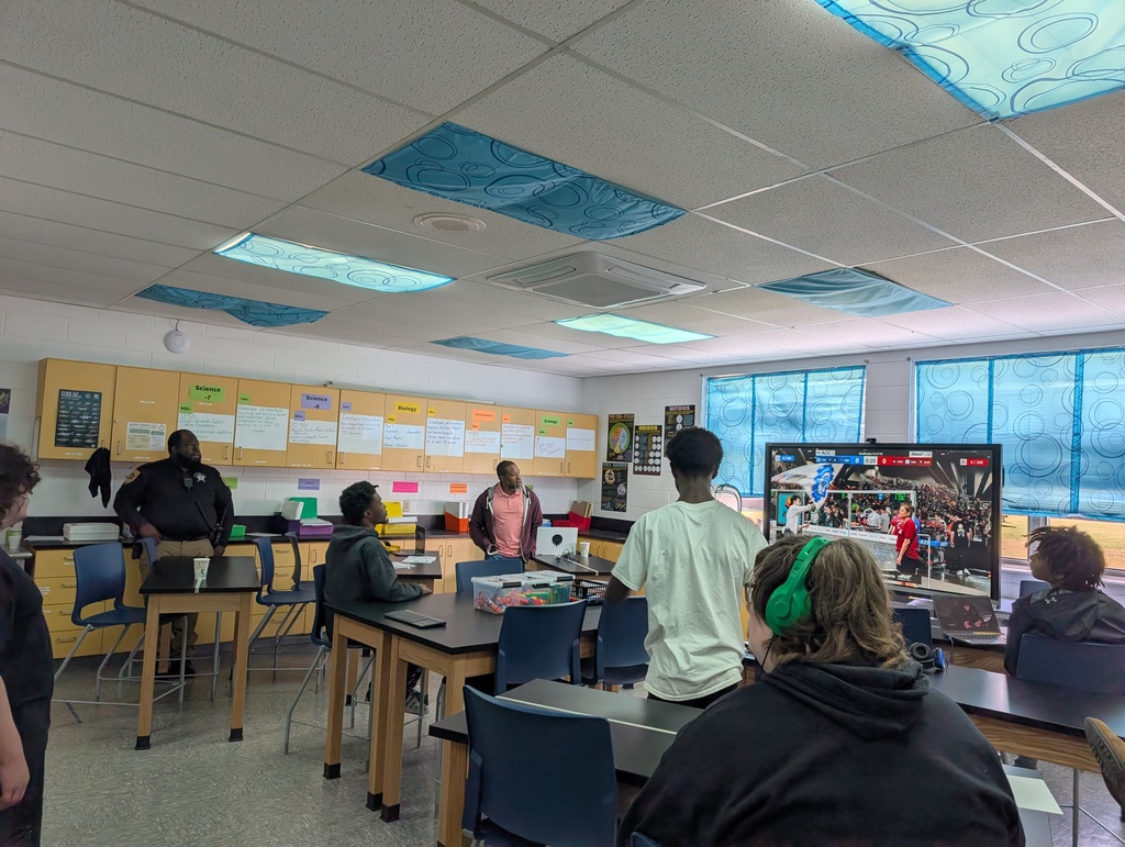 students in a classroom watching a robotics competition on a digital board