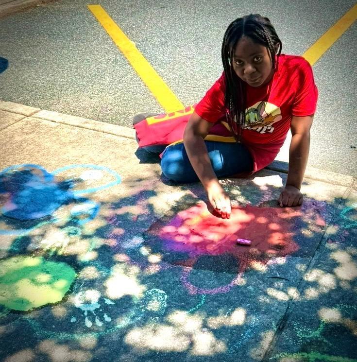 young girl creates images on sidewalk with chalk