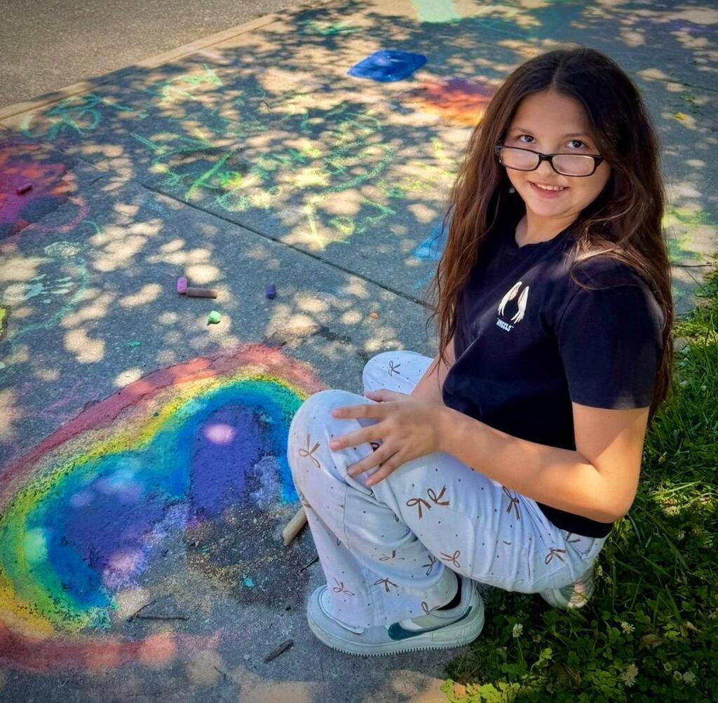 young girl creates images on sidewalk with chalk