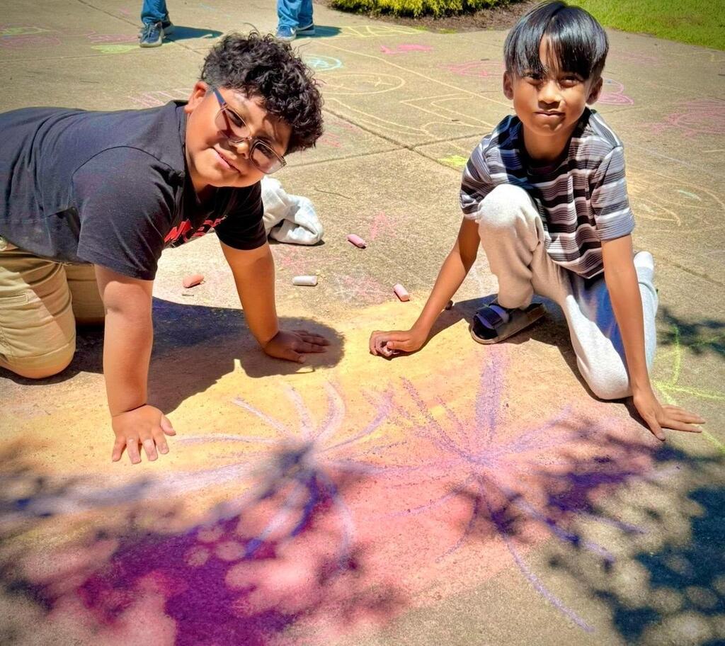 young boys create images on sidewalk with chalk