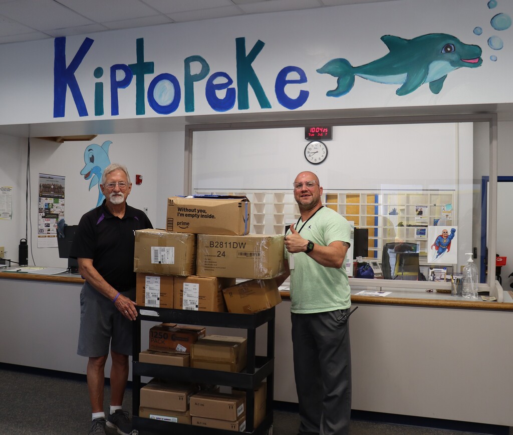 two adults post with donated school supplies in boxes.