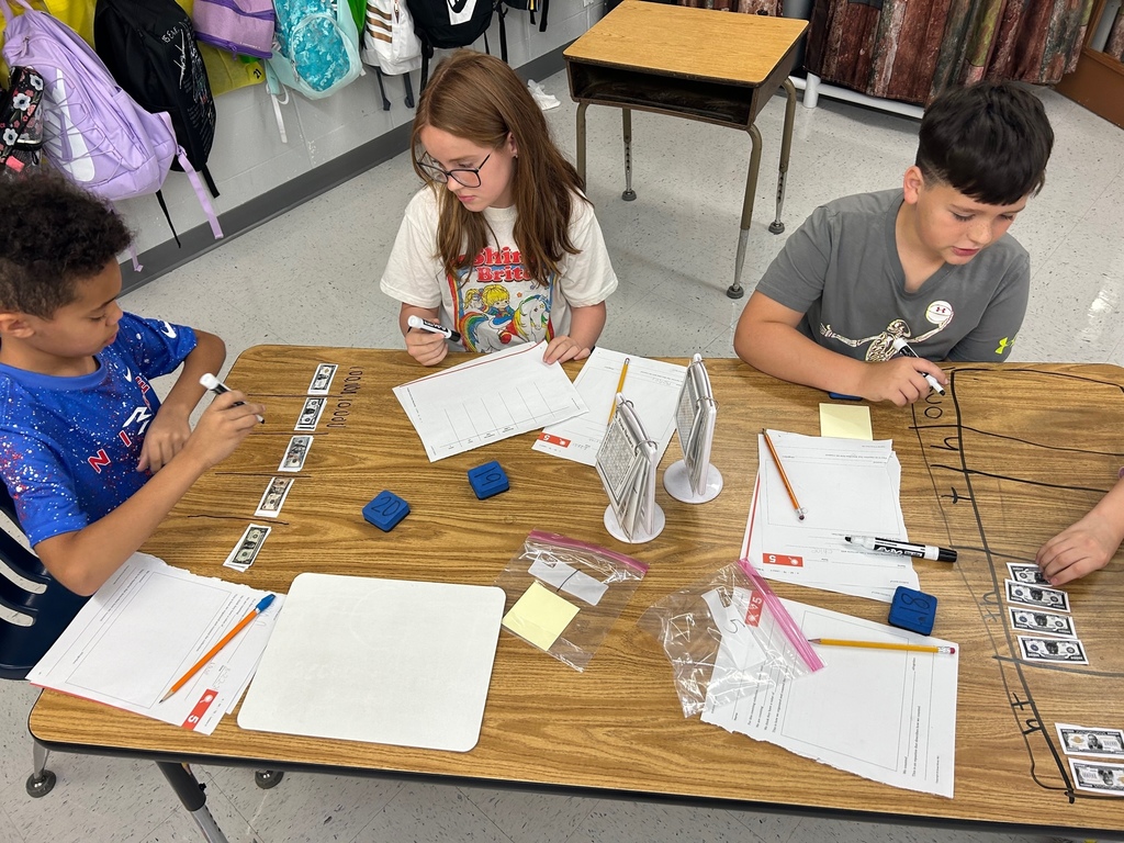 students in a classroom working with money manipulatives to count base ten system