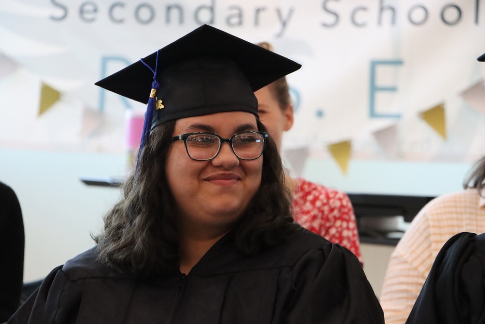 A female with glasses smiling wearing a graduation gown and cap
