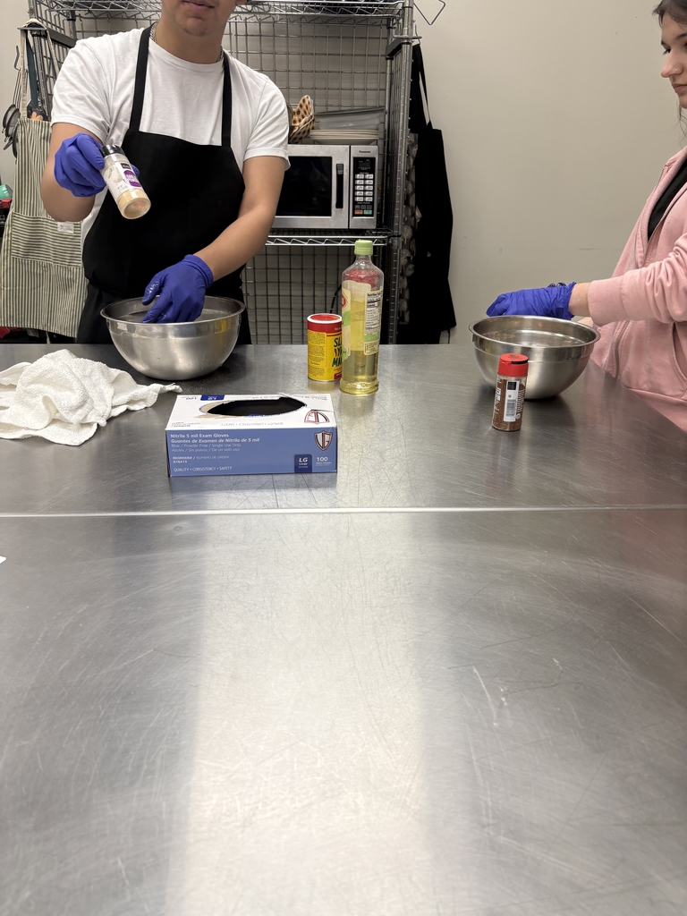 Image of students prepping food on a stainless steel table. 