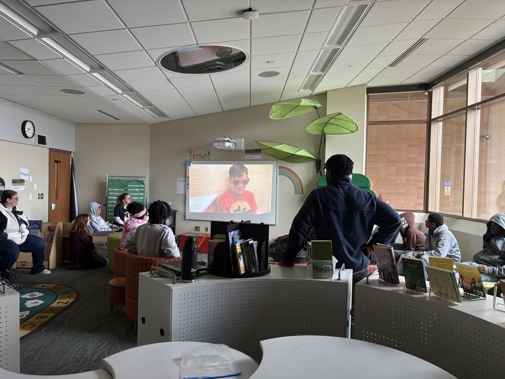 Image of students and staff sitting around watching a presentation on a screen.