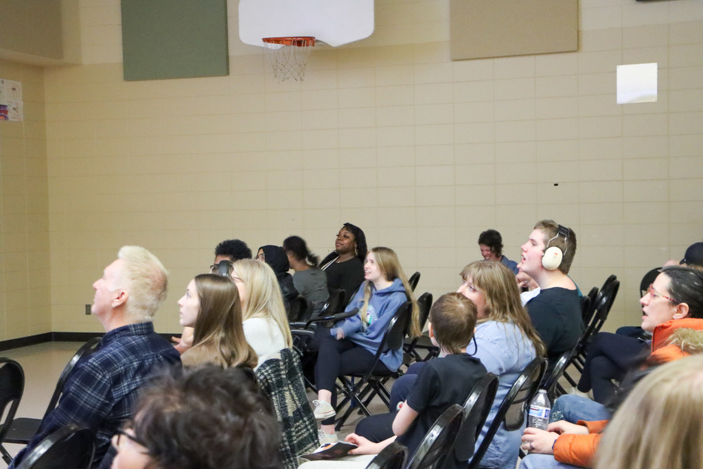 Image of students and staff sitting on chairs as they watch a video. 