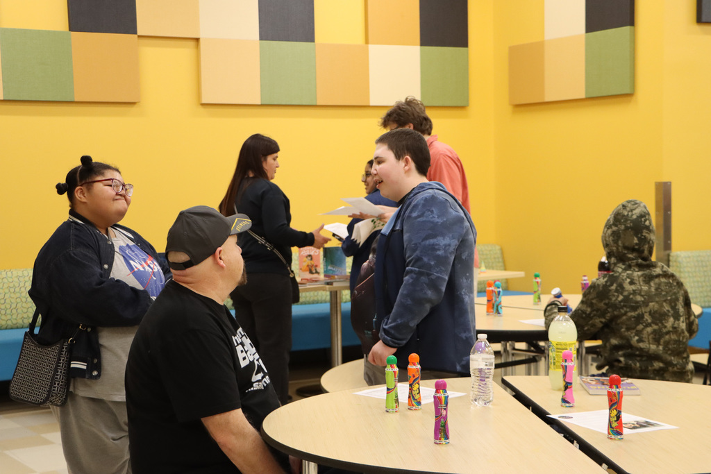 Image of students, staff, and parent talking to each other in the lunchroom while bingo is going on.