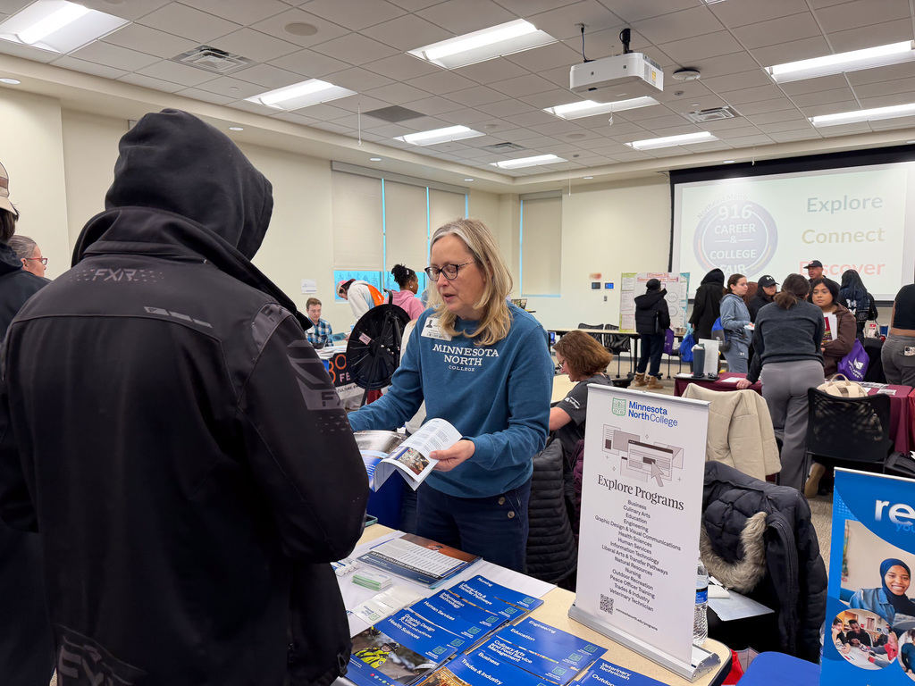 A student speaking to a college vendor who is showing them a booklet.