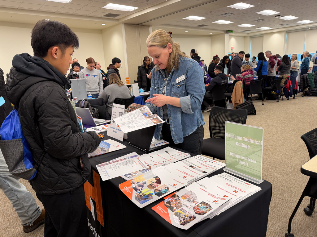 A student talking to a technical college vendor who is showing them a pamphlet.