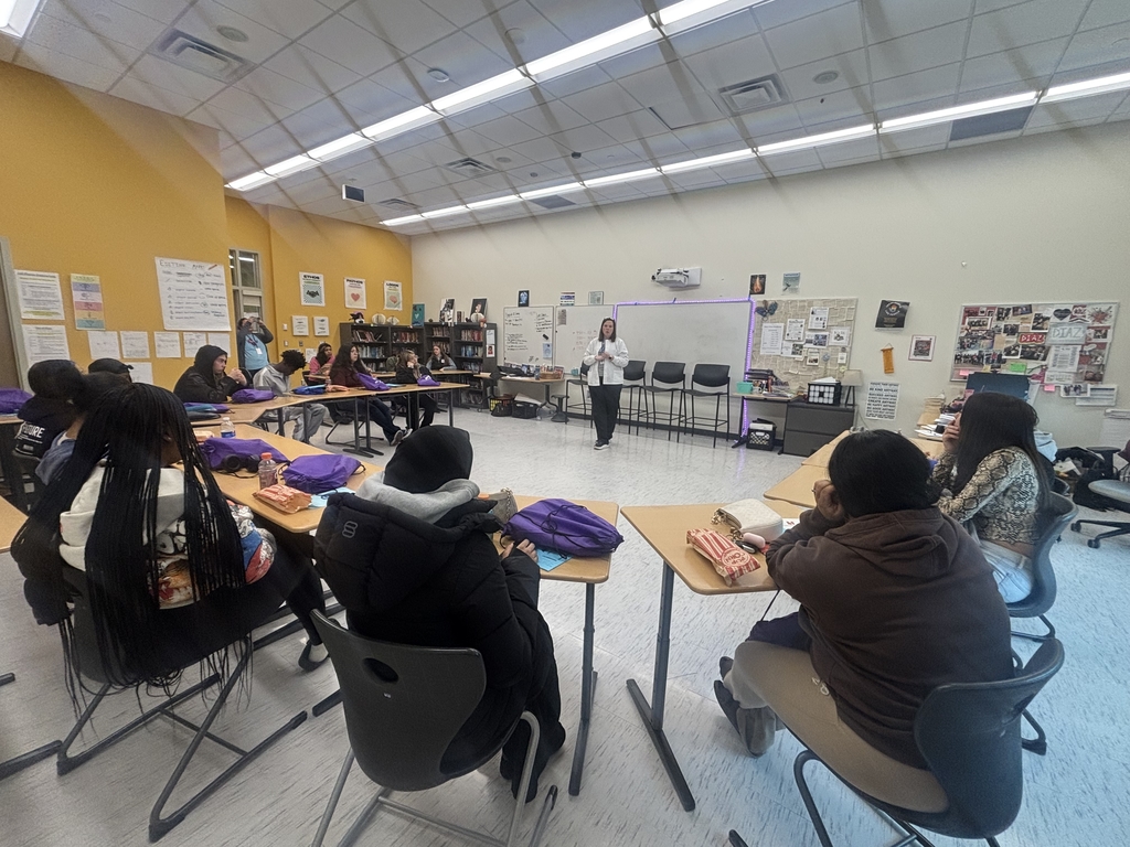 Students sitting in a classroom and listening to a career professional talk about their career. 