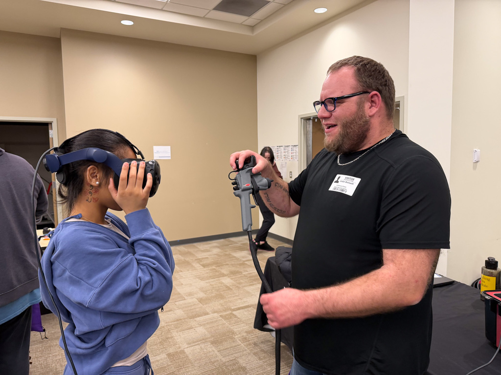A student trying on virtual reality headset while a career professional holds the controller for them to use.